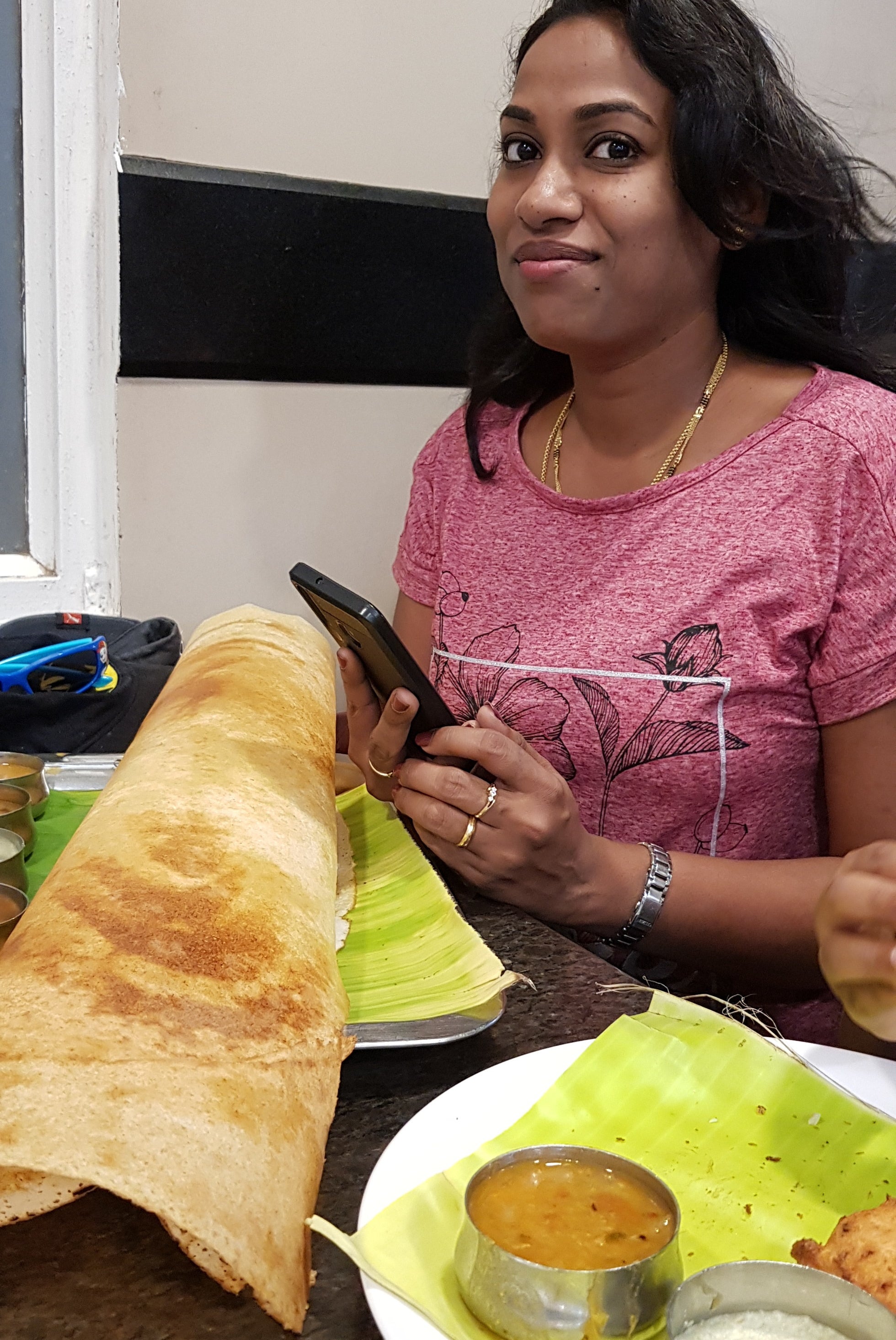 A woman holds her phone while sitting at a table which has dosa on it