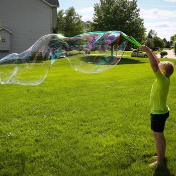 reviewer photo of their child using the bubble wand to blow a giant bubble