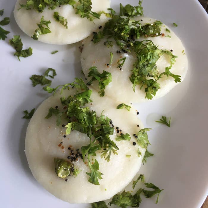 Three idlis, which are white in color, are garnished with coriander leaves and served on a white plate