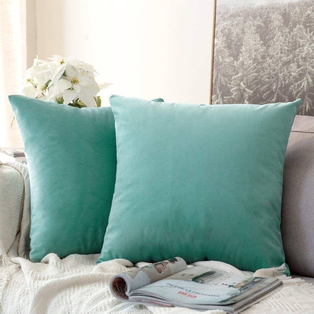 Two turquoise velvet cushion covers on a sofa next to a magazine