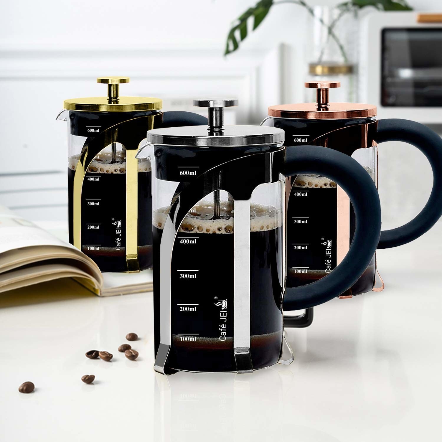 A French Press coffee maker in 3 colours on a table with coffee beans
