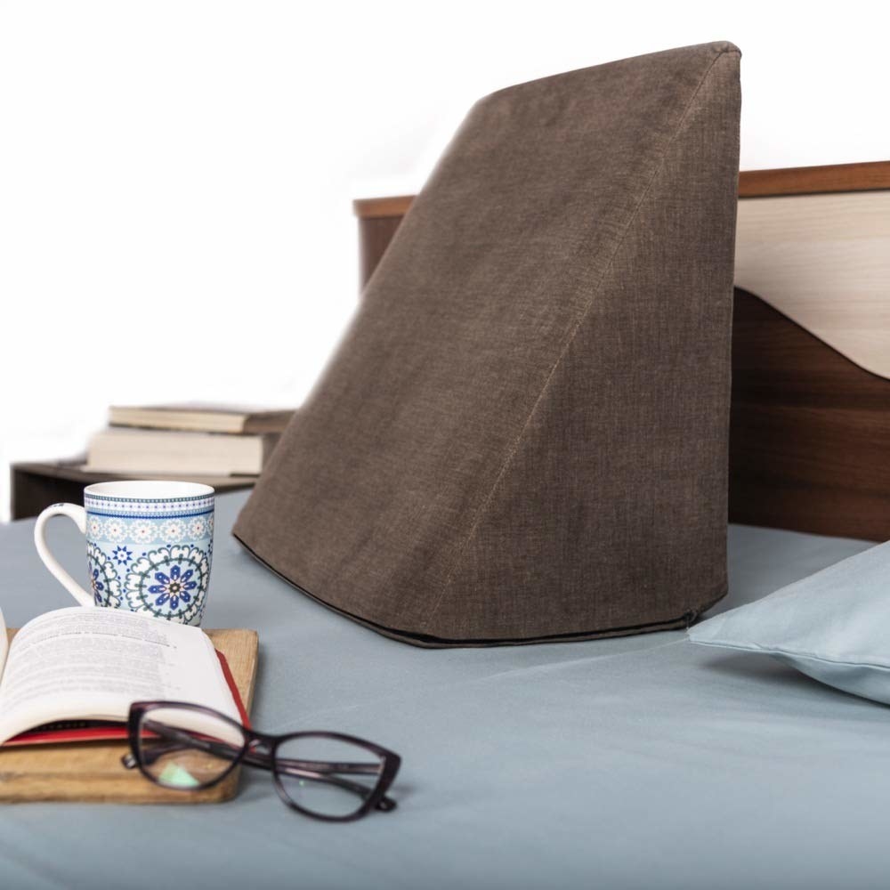 A wedge pillow on a bed next to a mug and a book