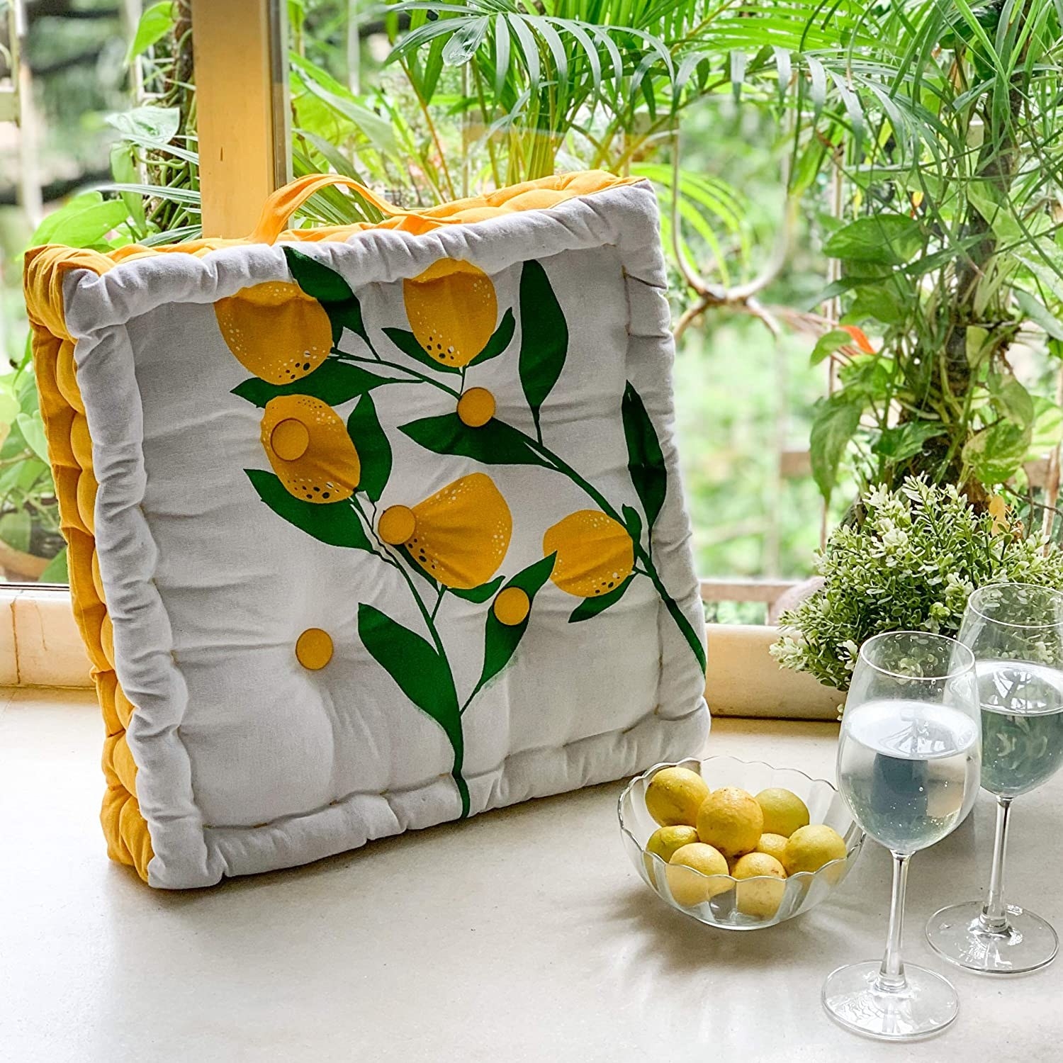 A floor pillow with lemons and two wine glasses beside it