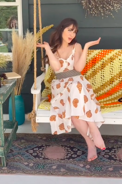Zooey sitting barefoot on a porch bench swing in a printed dress