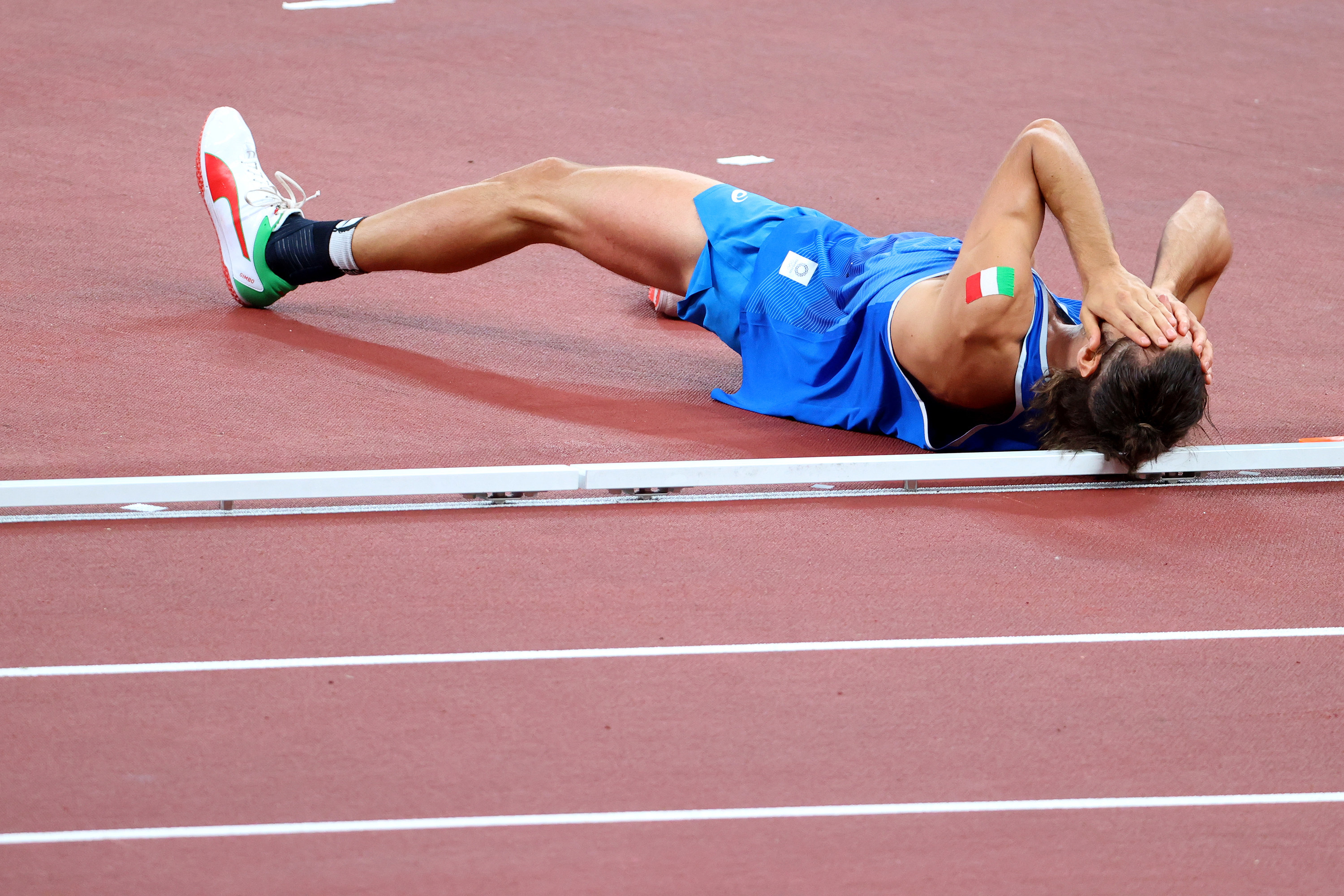  Tamberi lies on his back on the track and covers his eyes with his hands