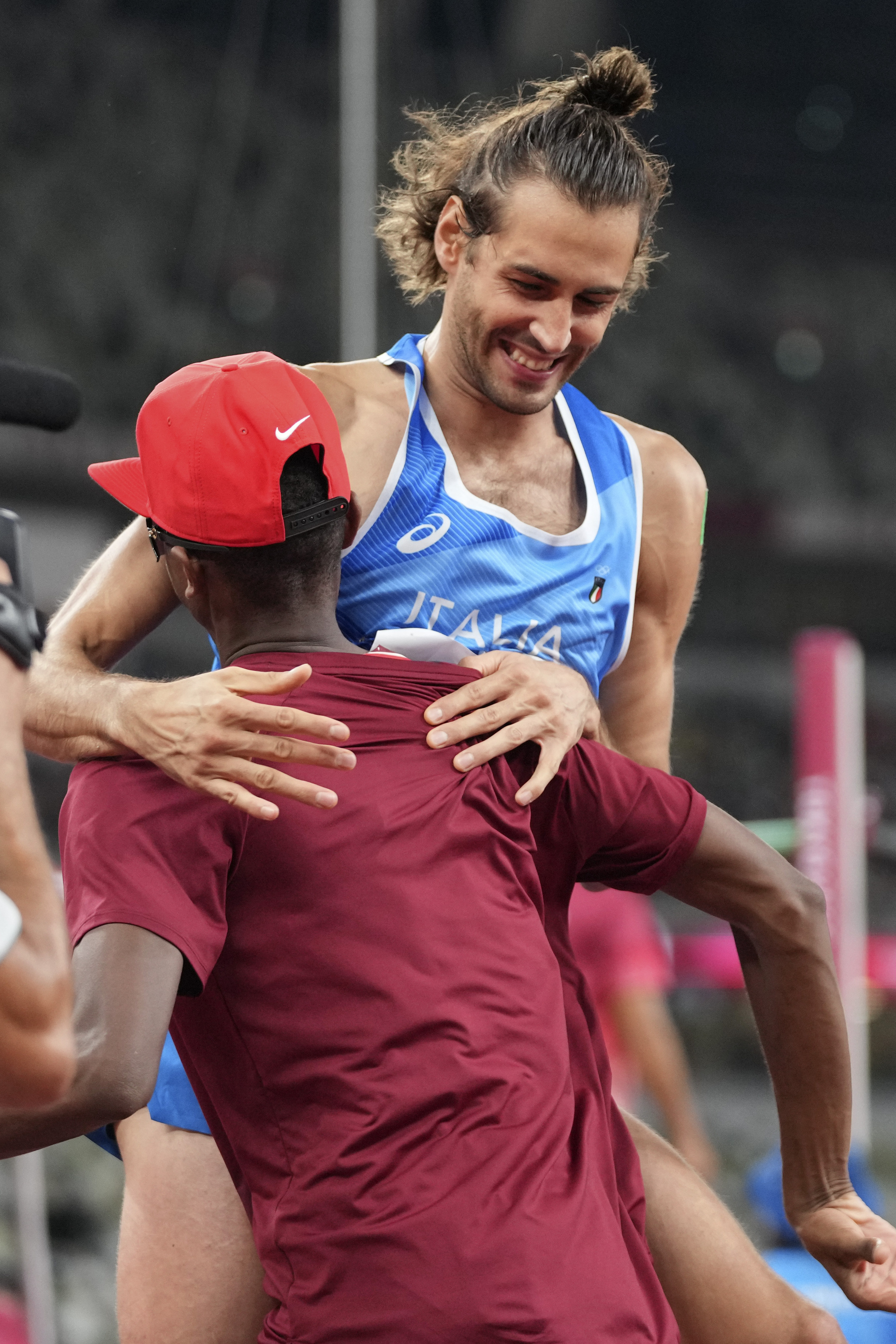 Tamberi smiles as he jumps and holds Barshim by the shoulders