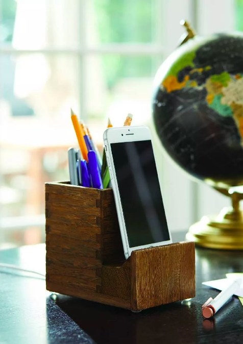 The pencil cup holding writing utensils and a smartphone held upright in the stand