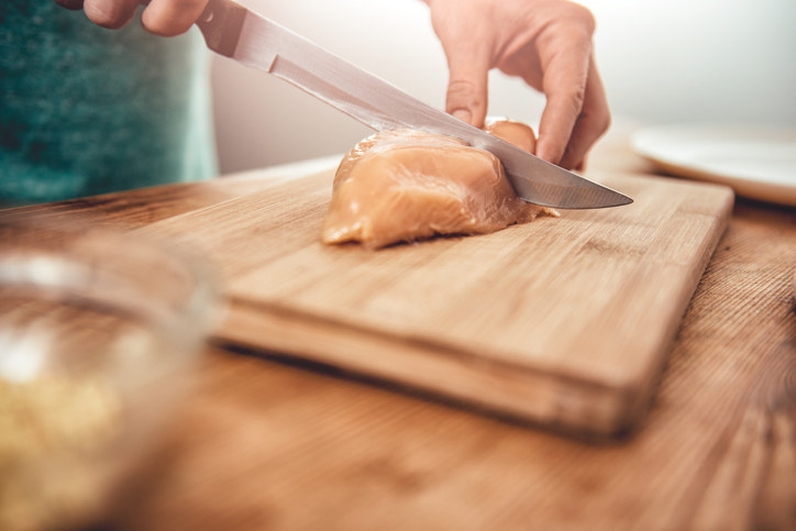 A person cutting a chicken breast on a cutting board