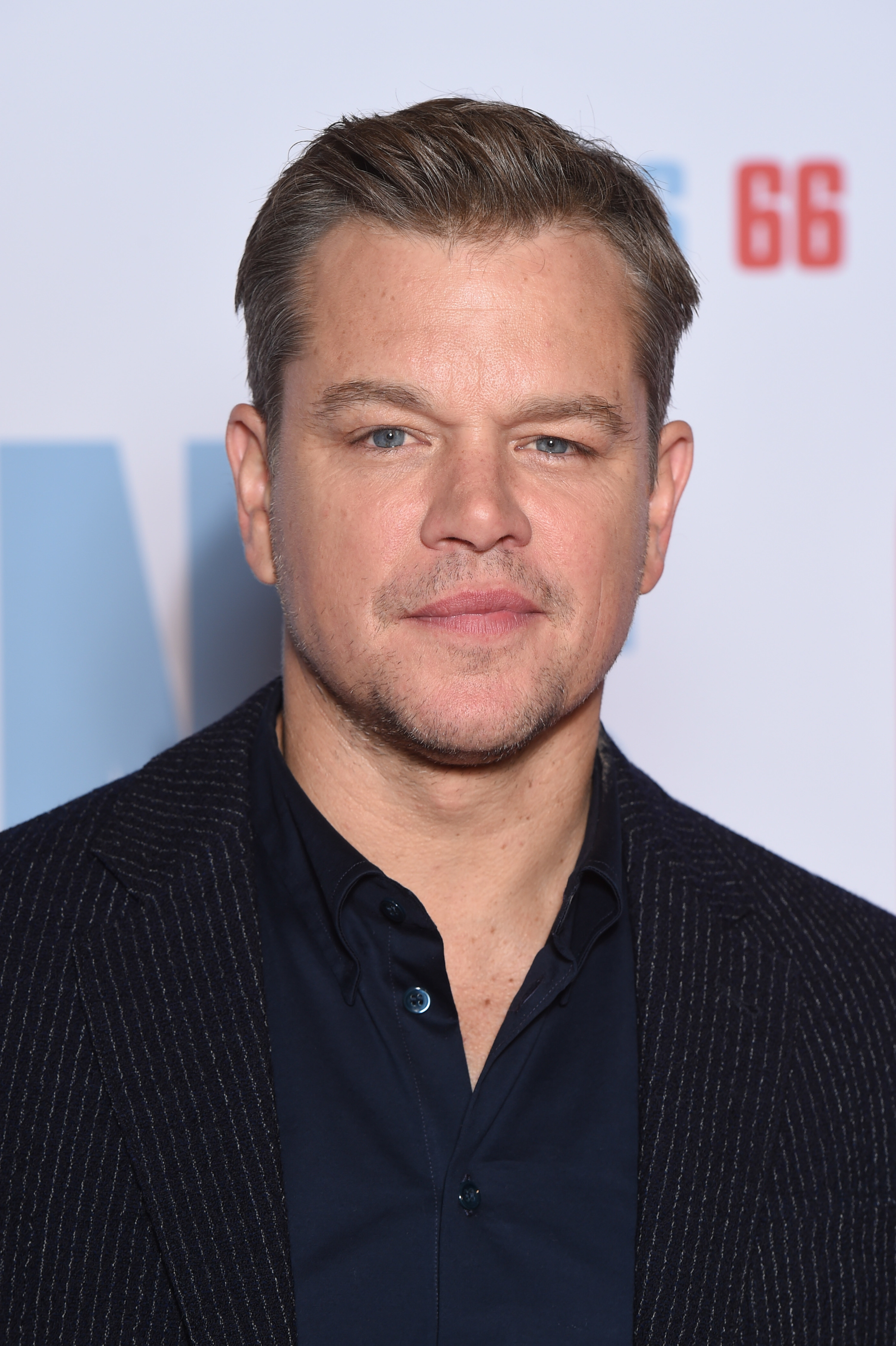 Damon poses for a photo while wearing a suit and button-down shirt at a movie premiere