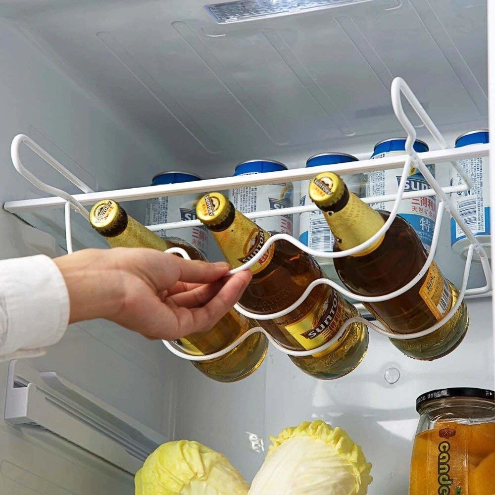 A hand pulling out the bottle rack in a fridge with 3 bottles on it