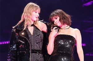 Selena Gomez (brown cropped hair) and Taylor Swift (blonde mid-length hair) standing together on reputation tour. Taylor's hand is resting on Selena's shoulder and both are smiling lovingly