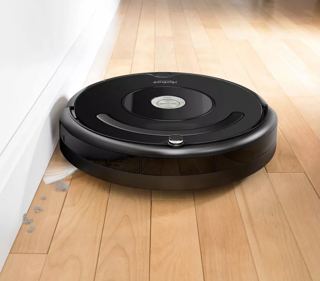 A black, wifi-controlled Roomba vacuum cleaning dust off a wooden floor