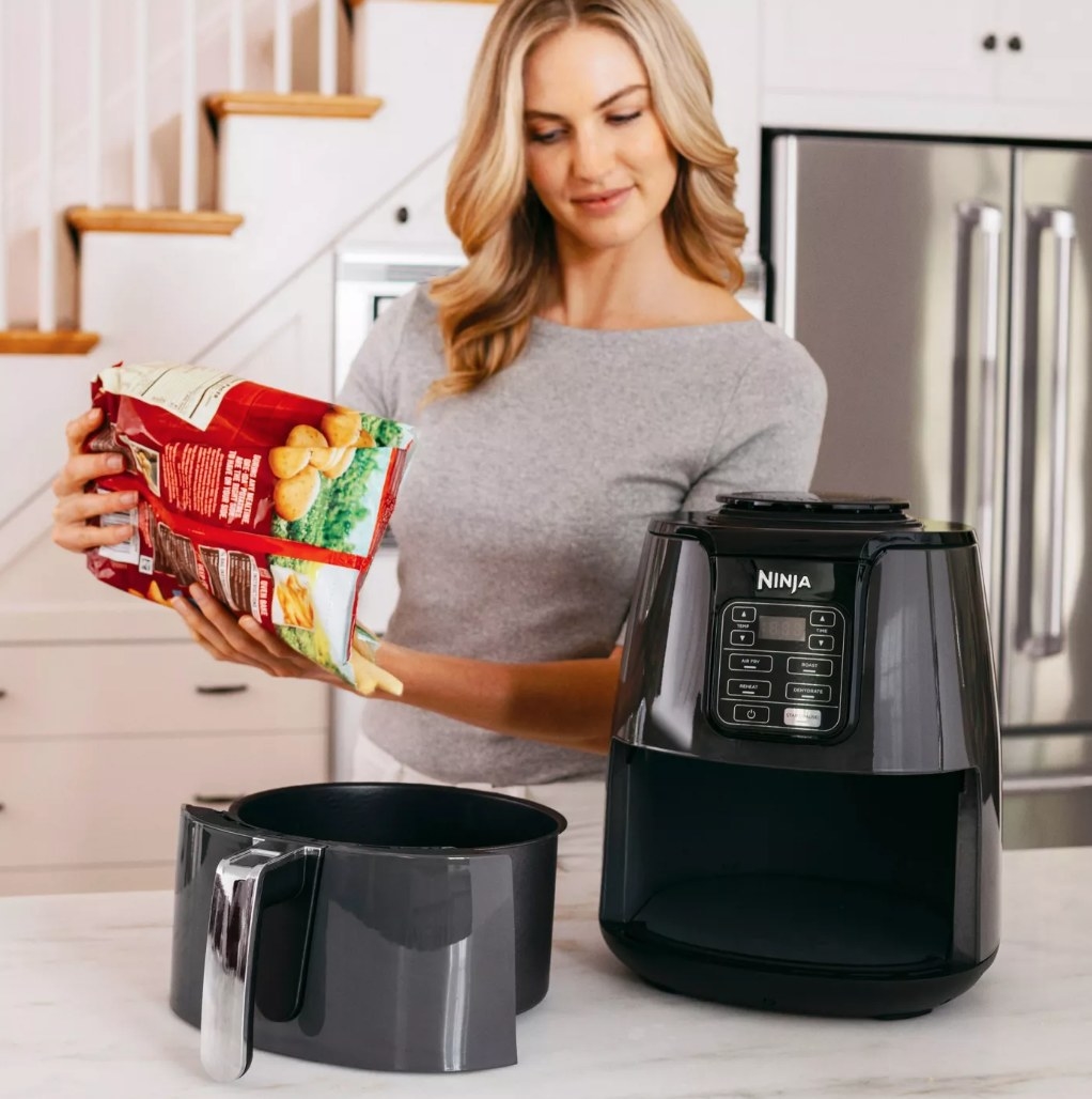 A model pouring frozen french fries into the black, Ninja 4-qt air fryer
