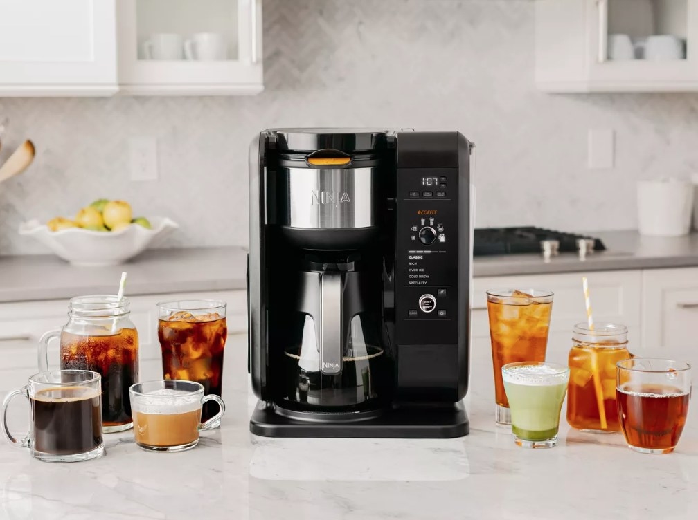 A black, Ninja hot &amp;amp; cold brew coffee maker on a kitchen counter next to several hot and cold coffee and tea beverages
