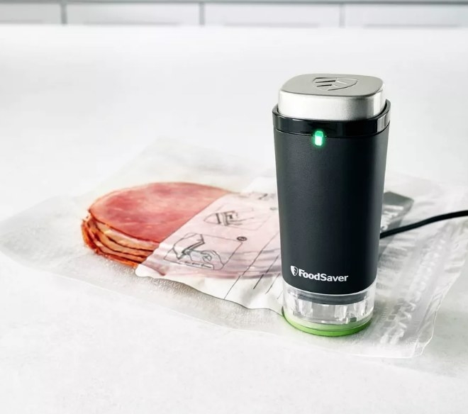 A black, handheld vacuum sealer being used on a FoodSaver bag to preserve meat