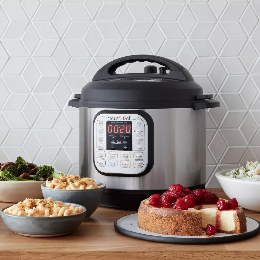 A silver/black, Instant Pot slow cooker on a counter surrounded by meals