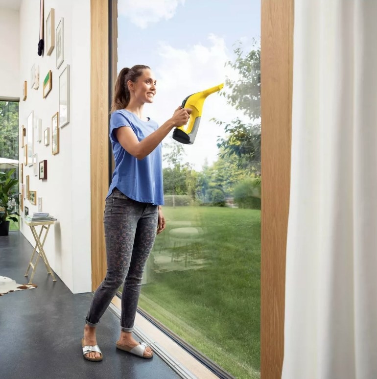 A model using a yellow, cordless window vacuum to clean the dirt off the floor-to-ceiling windows