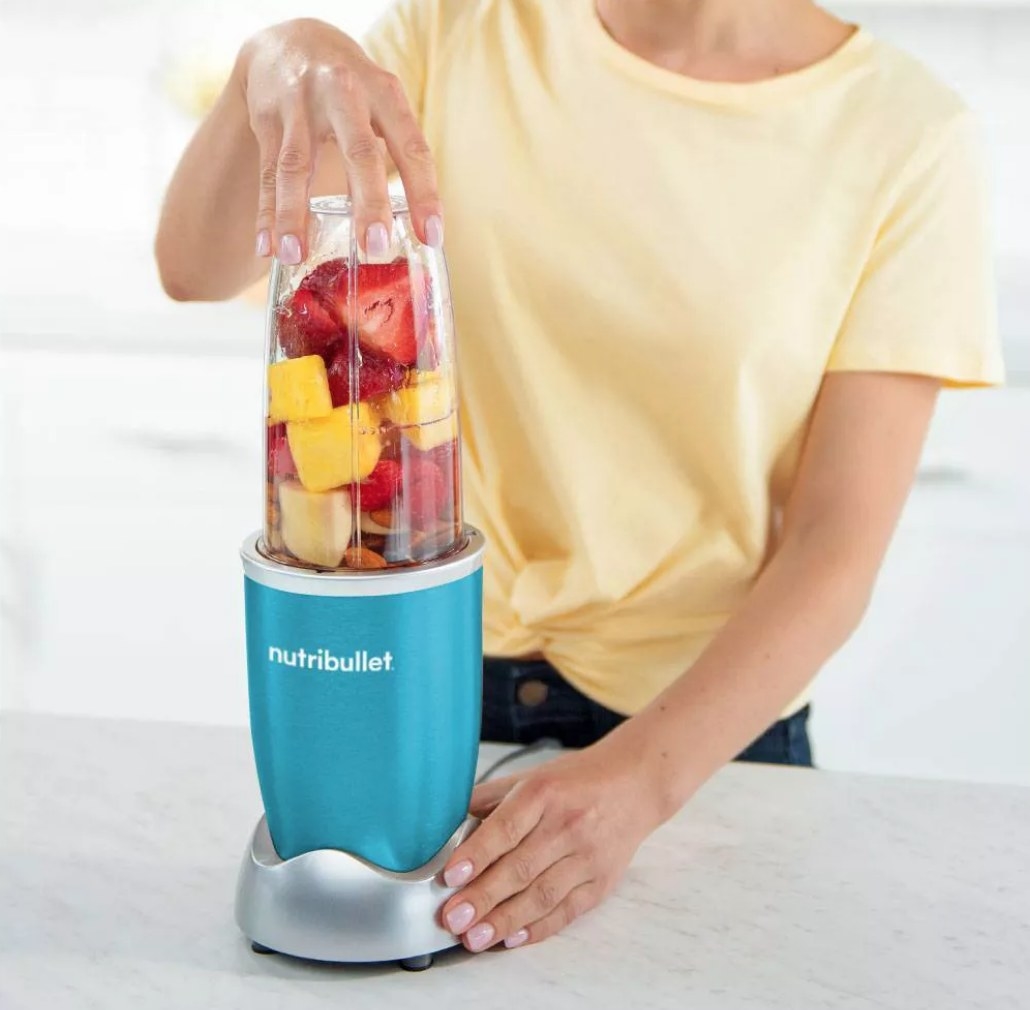 A model using a teal  Nutribullet to blend a single-serve smoothie