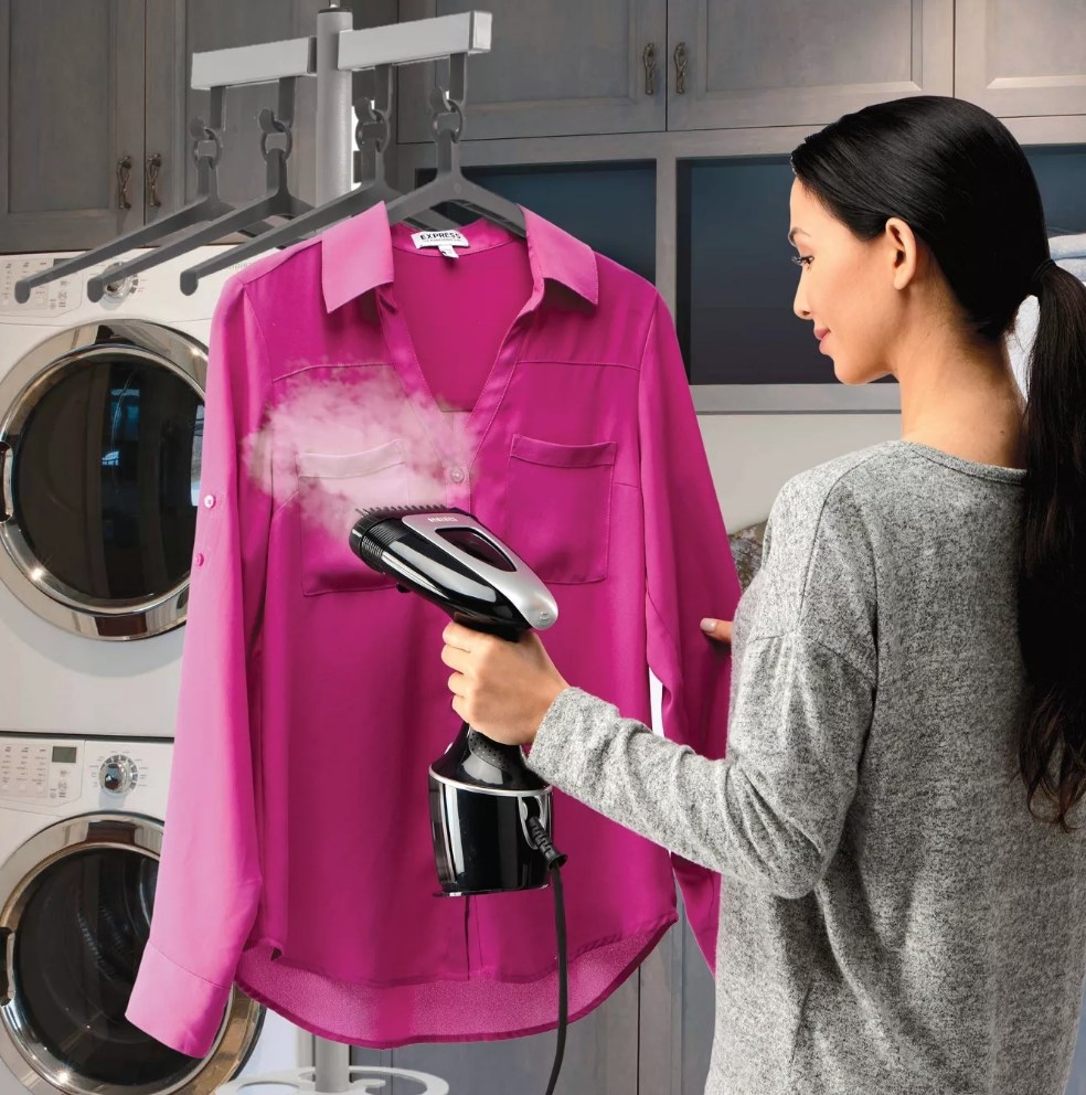 A model using a handheld garment steamer on a pink blouse