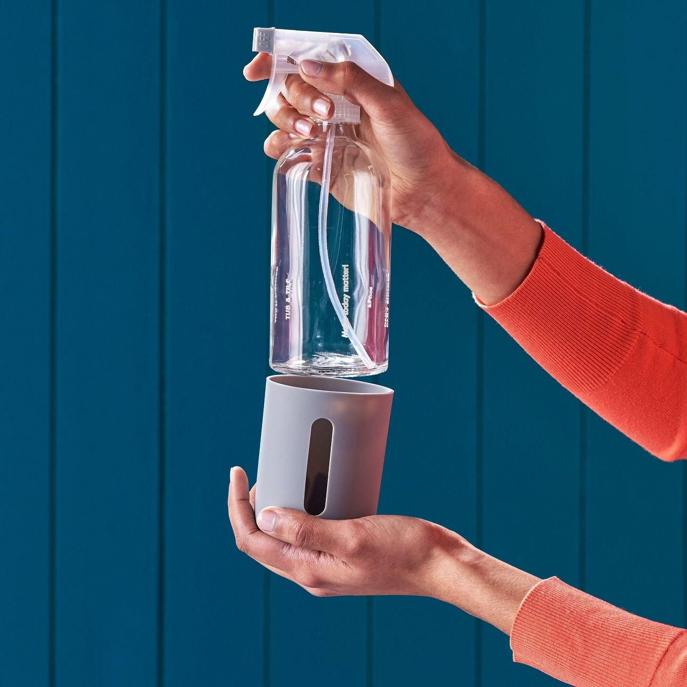 hands holding a reusable glass spray bottle and gray silicon sleeve