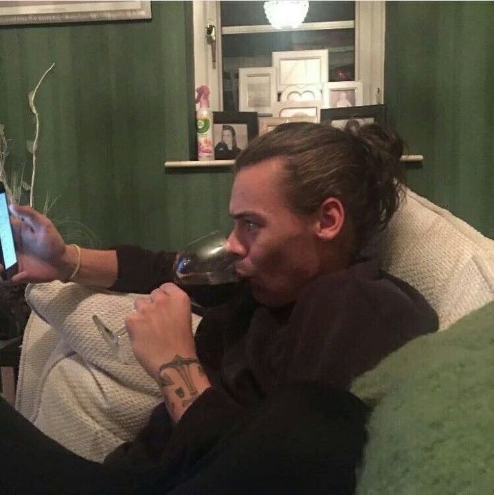 Harry Styles staring at his phone while sipping a glass of red wine