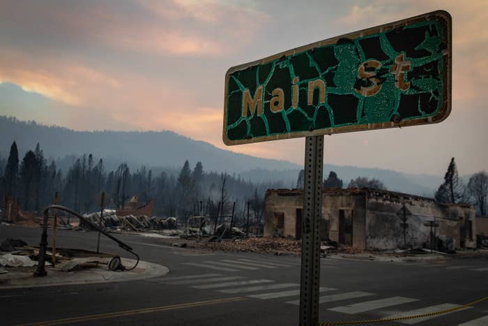A gnarled street sign that says Main St with a burned out building and a bent streetlight in the background