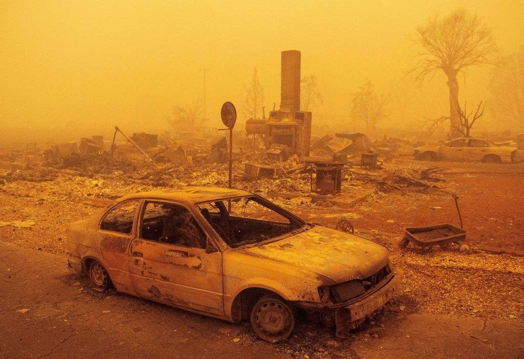 A burned out car and destroyed home under an orange haze