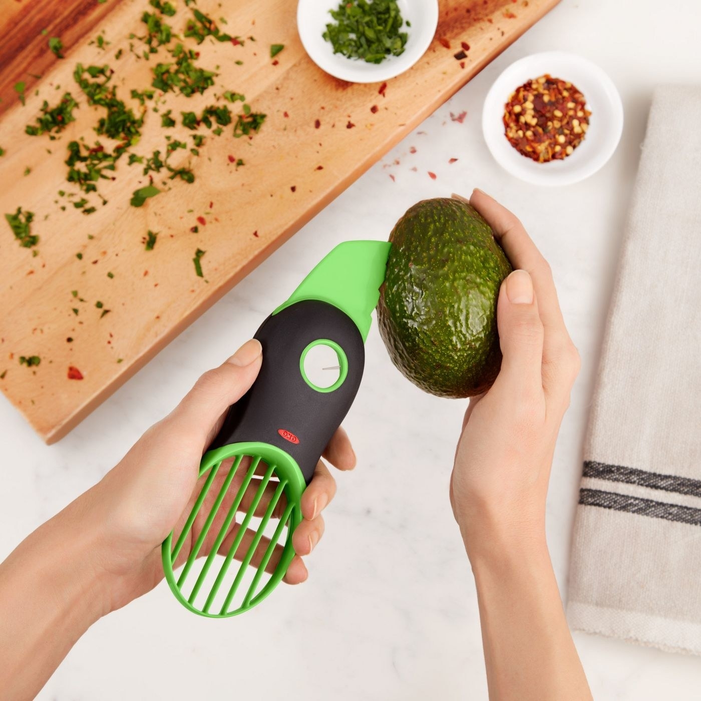 hands holding an avocado and a green and black avocado slicer