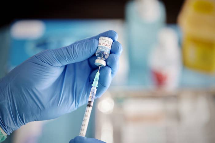 A person wearing blue medical gloves inserts a needle in a vial