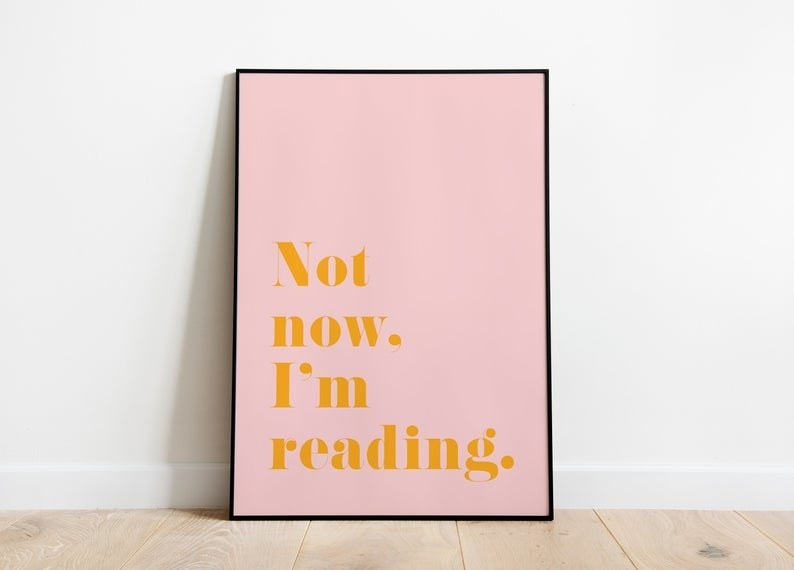 a pink wall art print in a black frame with deep mustard yellow lettering