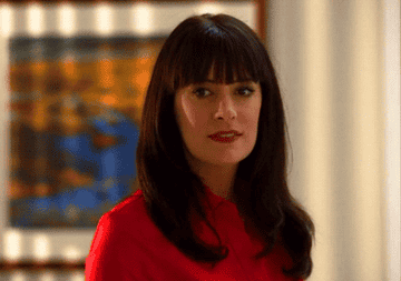 GIF of Emily Prentiss smiling, she is wearing a red shirt and has shoulder length hair