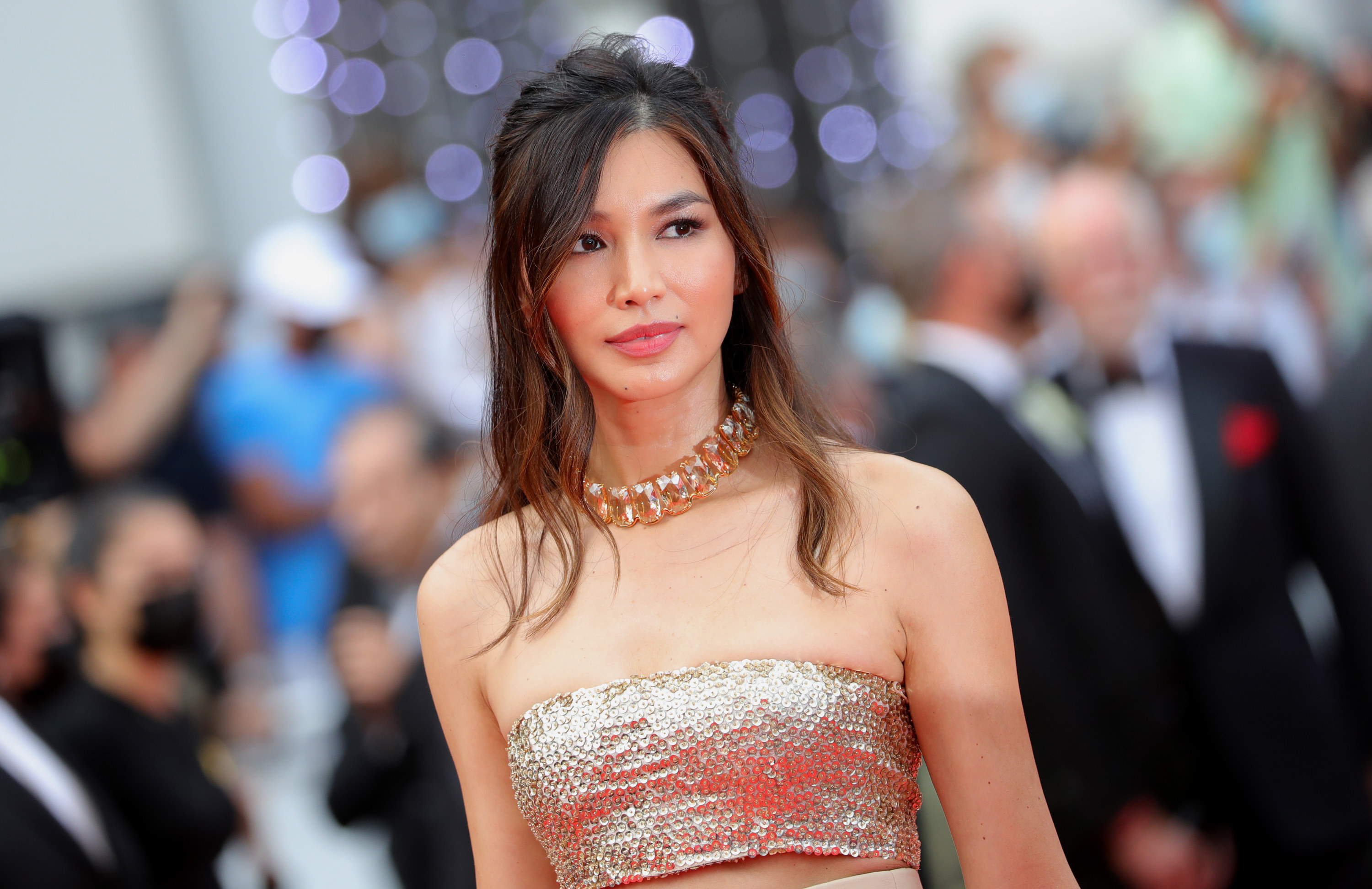 Gemma looks into the distance while wearing a strapless gold sequined top at an event