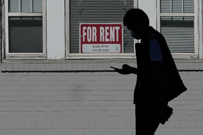 A man walks in front of a "for rent" sign in a window of a residential property