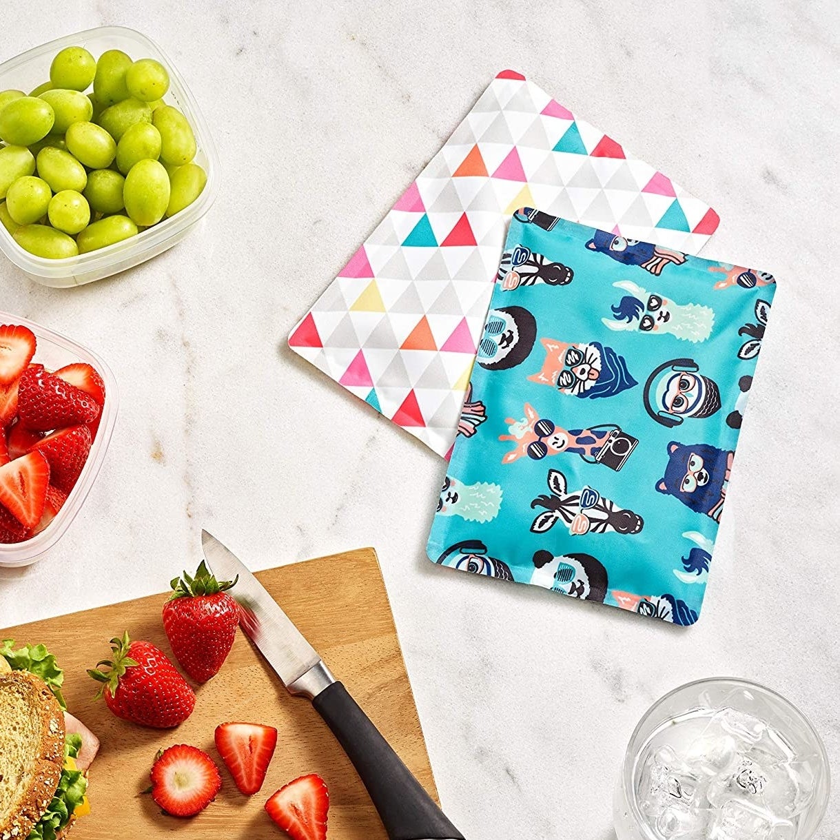 two vibrant ice packs on a table next to a cutting board and glass of water