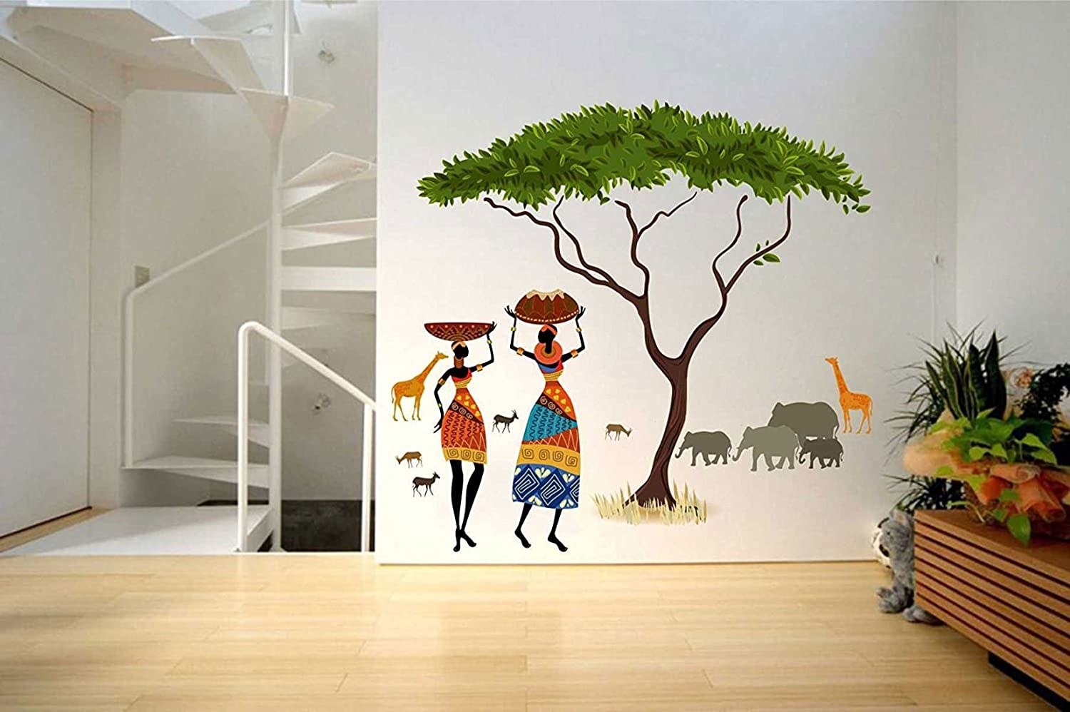 A wall decal with a large tree, giraffes, elephants and two women carrying baskets over their head