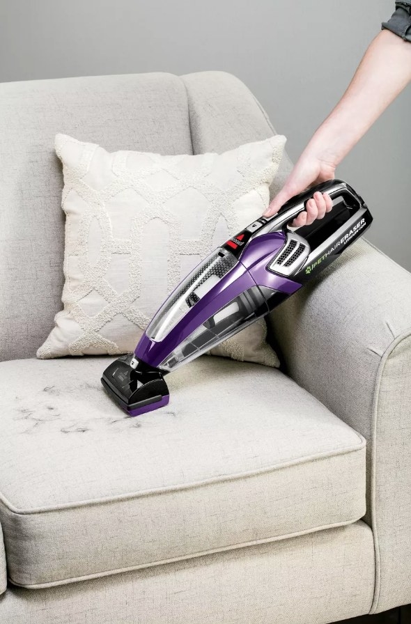 Model using purple Bissell handheld vacuum to clean pet hair from couch
