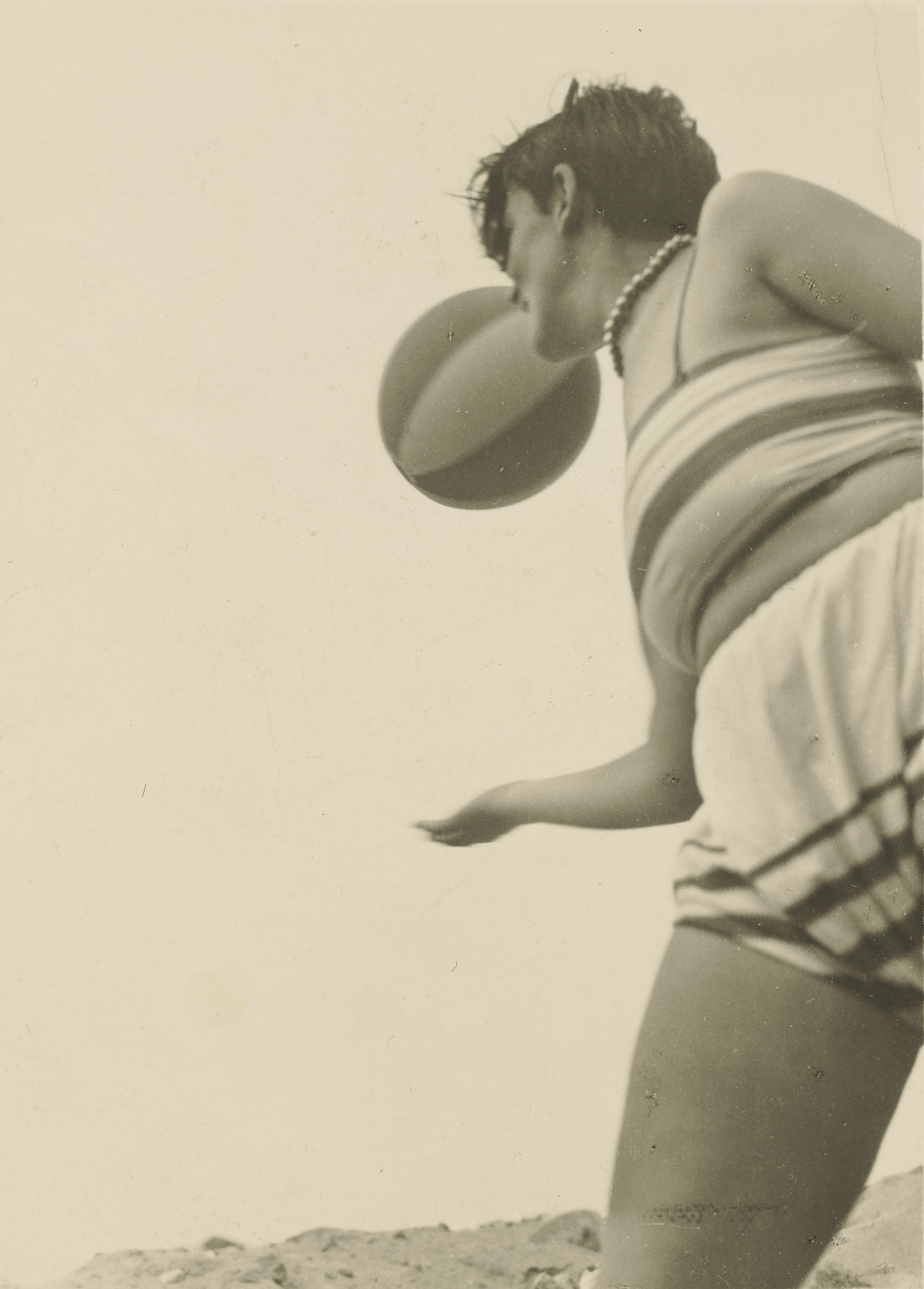 A woman in a striped suit bounces a beach ball, slightly off frame