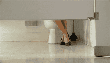 A woman peeing in a bathroom stall