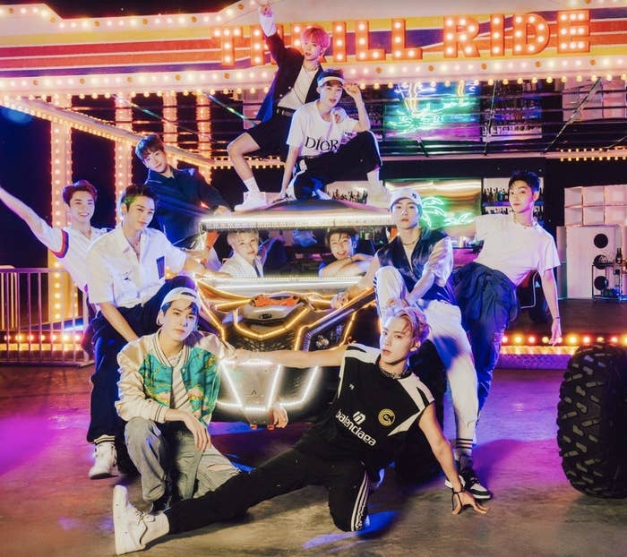 The members of the Boyz stand around a car in a bright arcade