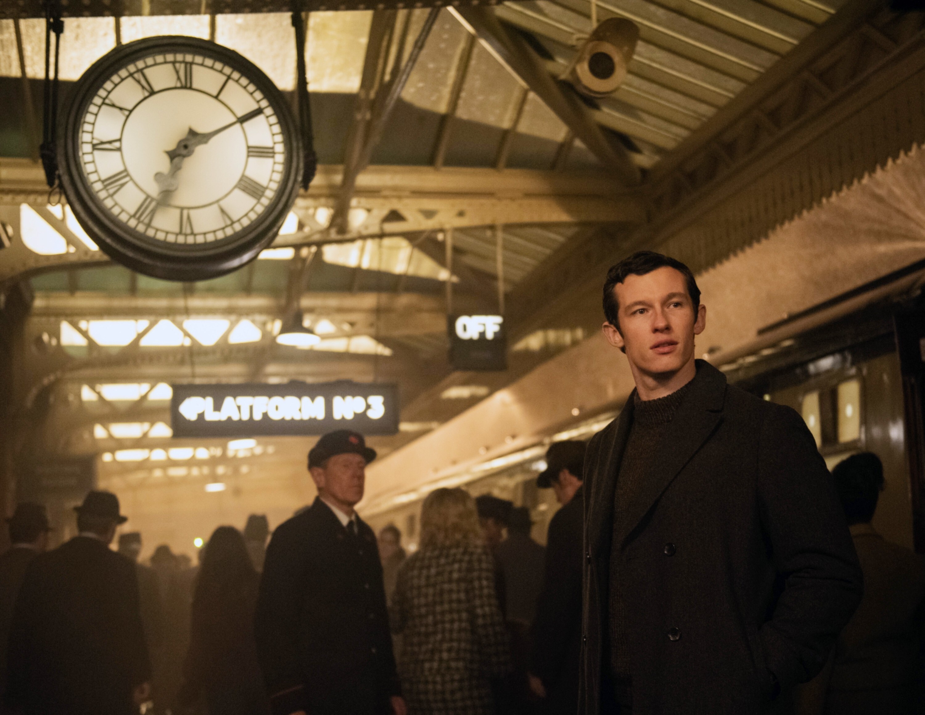 Anthony in a busy train station looking nervous, a large clock with Roman numerals above him to the left