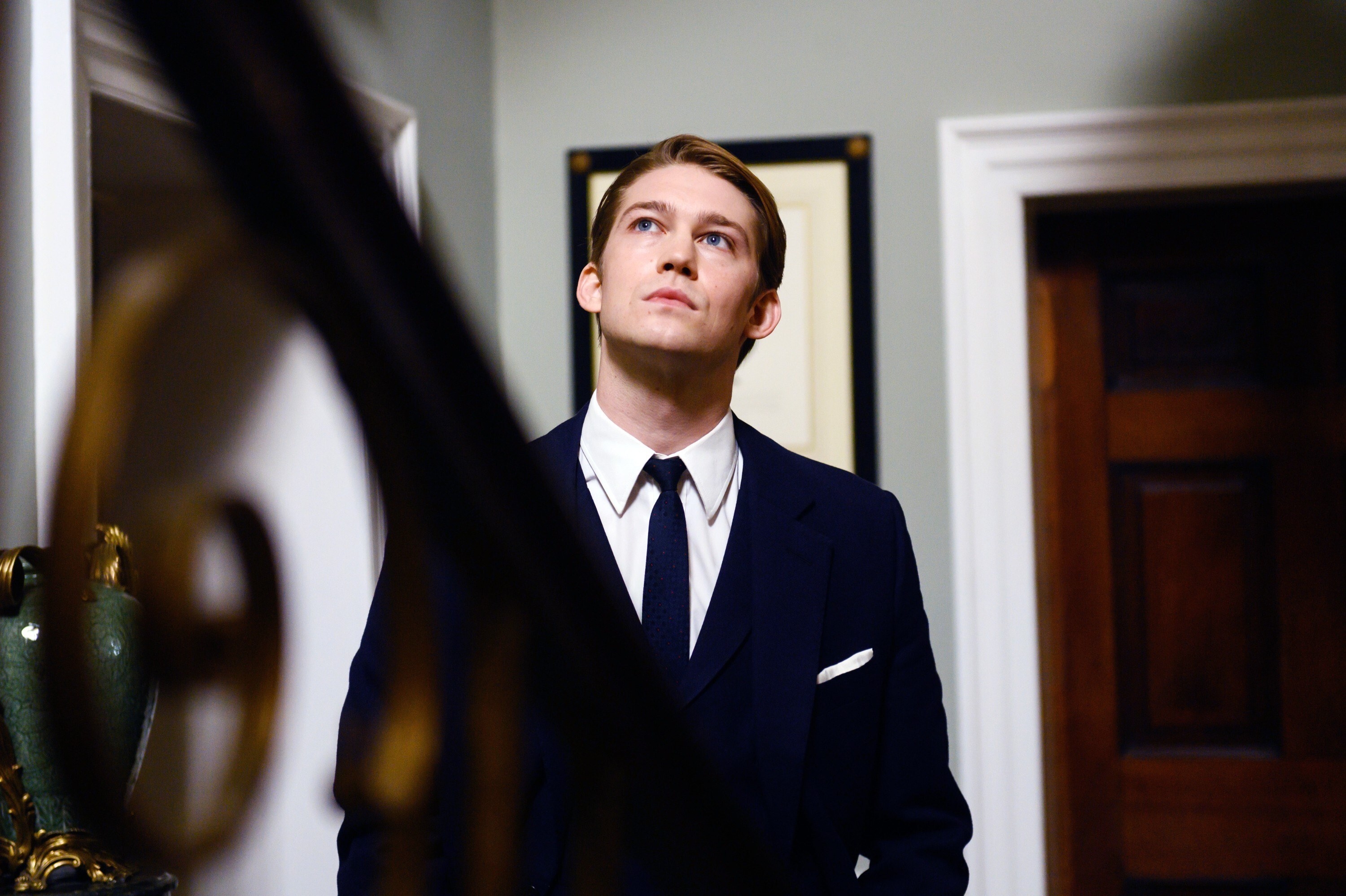 Joe Alwyn in a suit and tie looking up the stairs