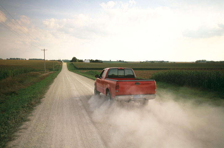 Red pick up truck traveling down dusty rural road