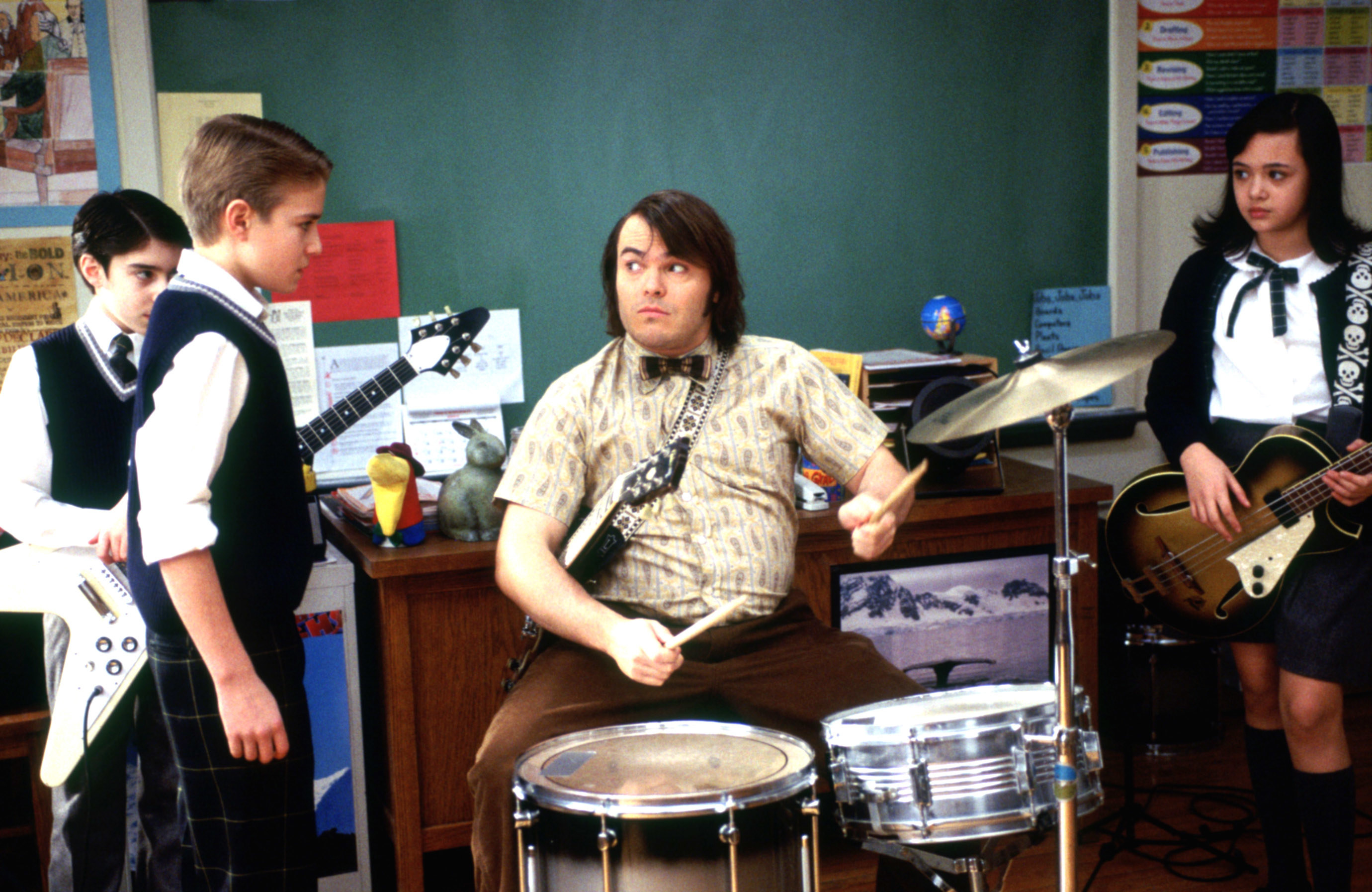 Jack Black sits at a drum set while the School of Rock children stand around him brandishing instruments