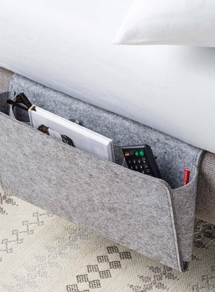 A close up of the bedside caddy tucked under the mattress, holding a remote and notebook