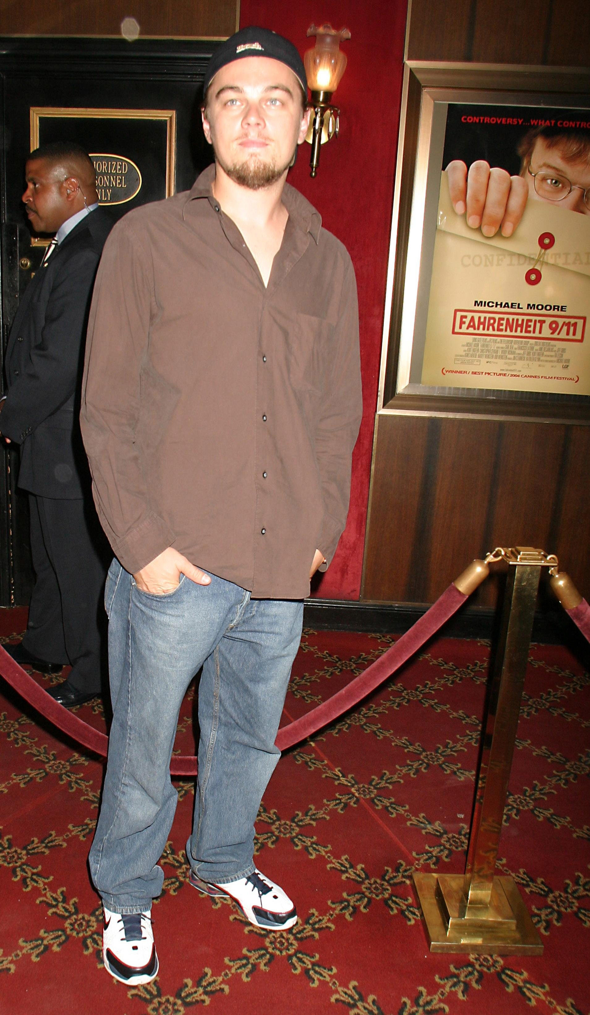 Leo is wearing a backwards baseball hat, an oversized brown button-down that is untucked, a pair of baggy light wash jeans, and Nike sneakers.