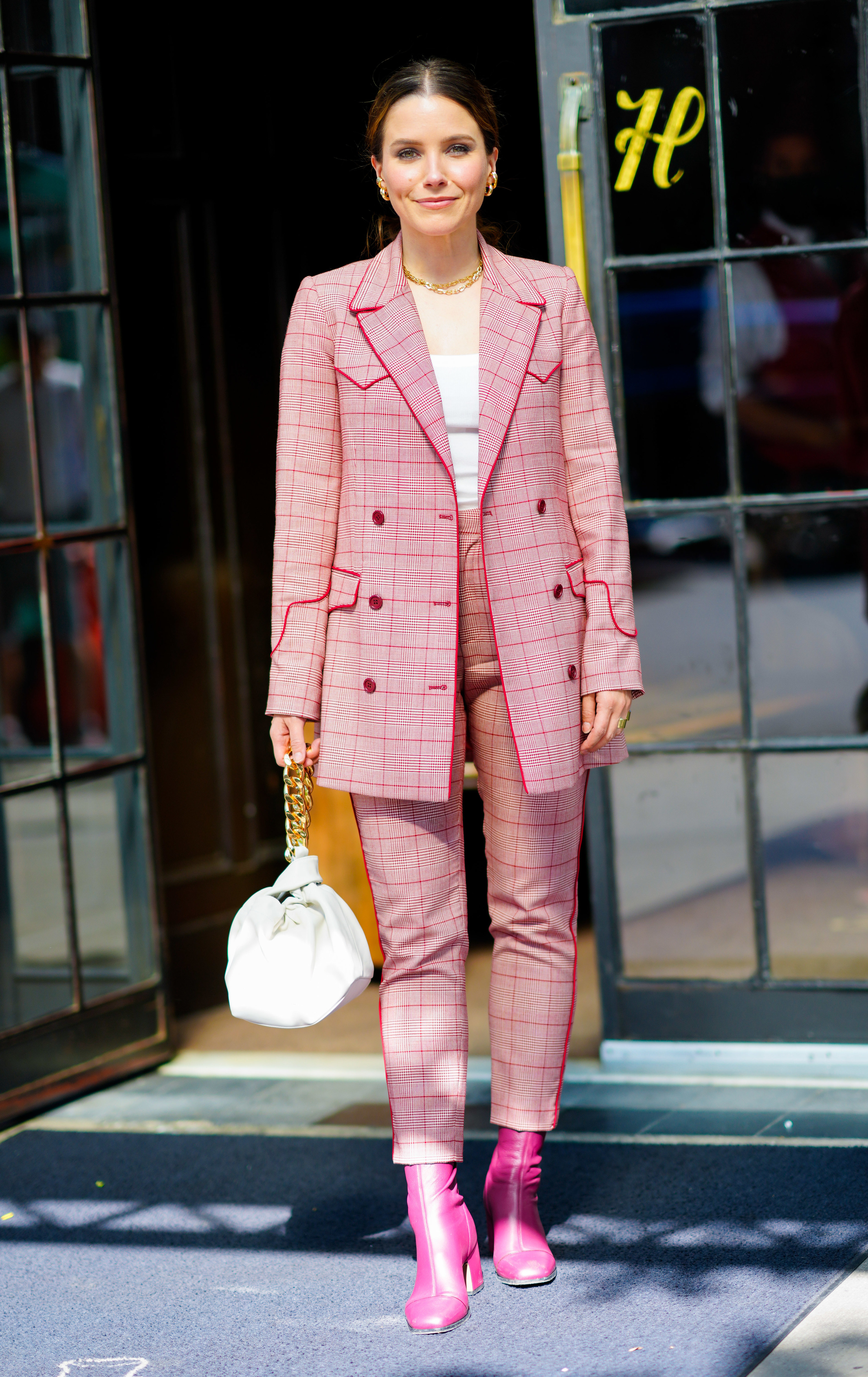 Sophia wears a pink plaid pantsuit with a gold chain necklace and bright pink boots.