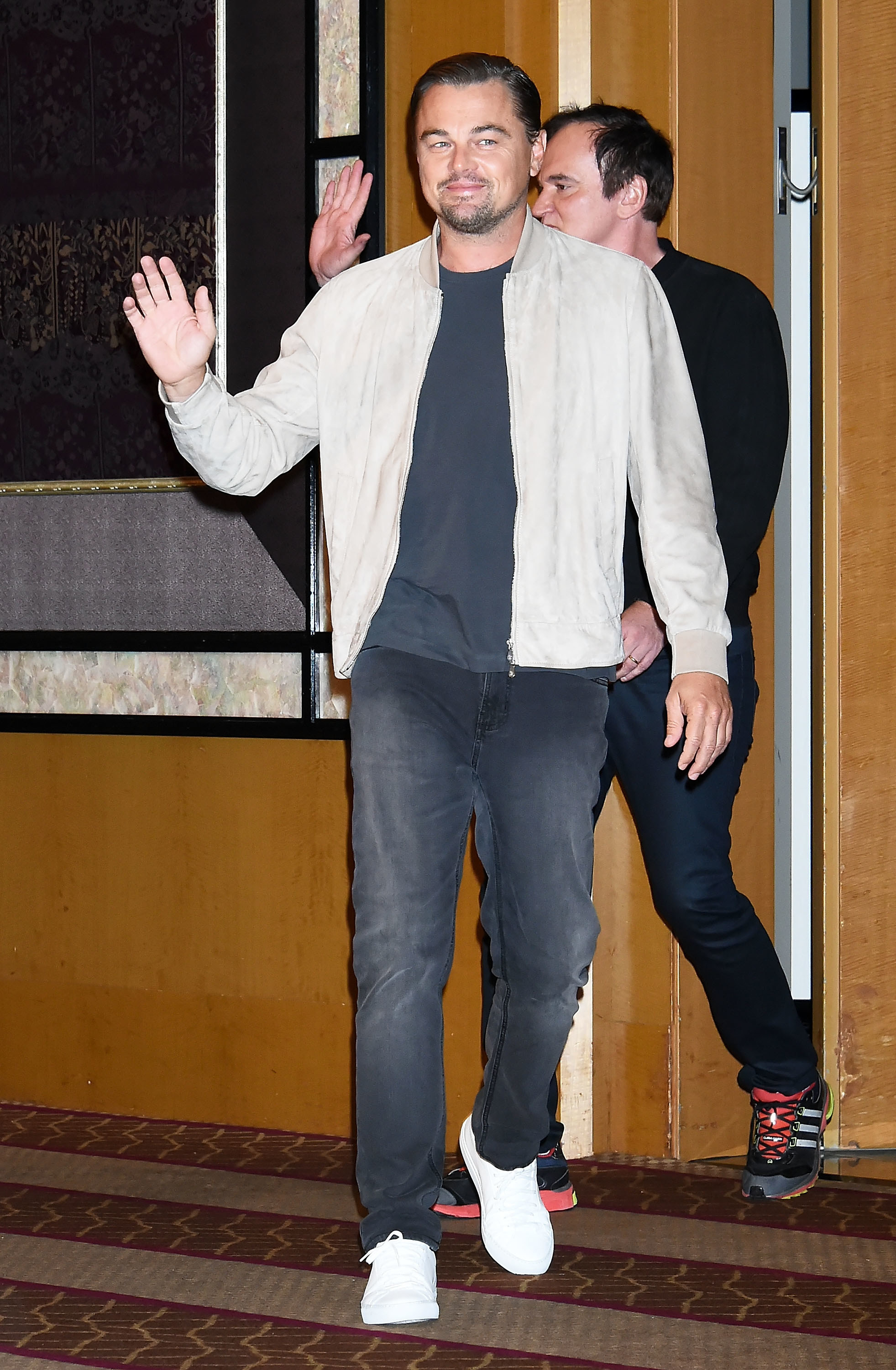 Leo wears a beige bomber jacket with a black t-shirt underneath. He&#x27;s also wearing black straight cut jeans and pure white sneakers.