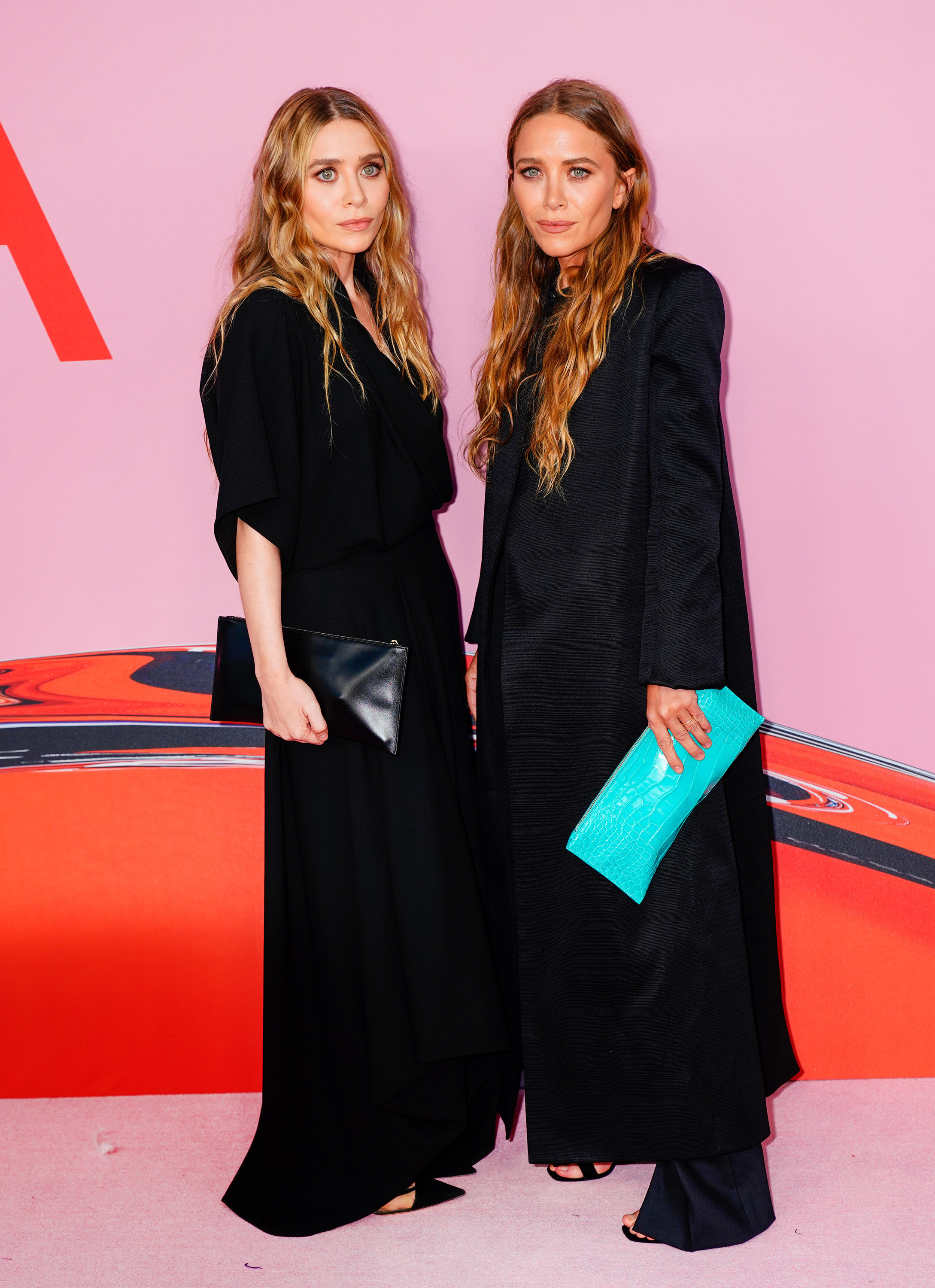 Mary-Kate and Ashley both wear billowy, long, dark colored dresses with sandals. Mary-Kate holds a bright colored snakeskin clutch while Ashley holds a black one.