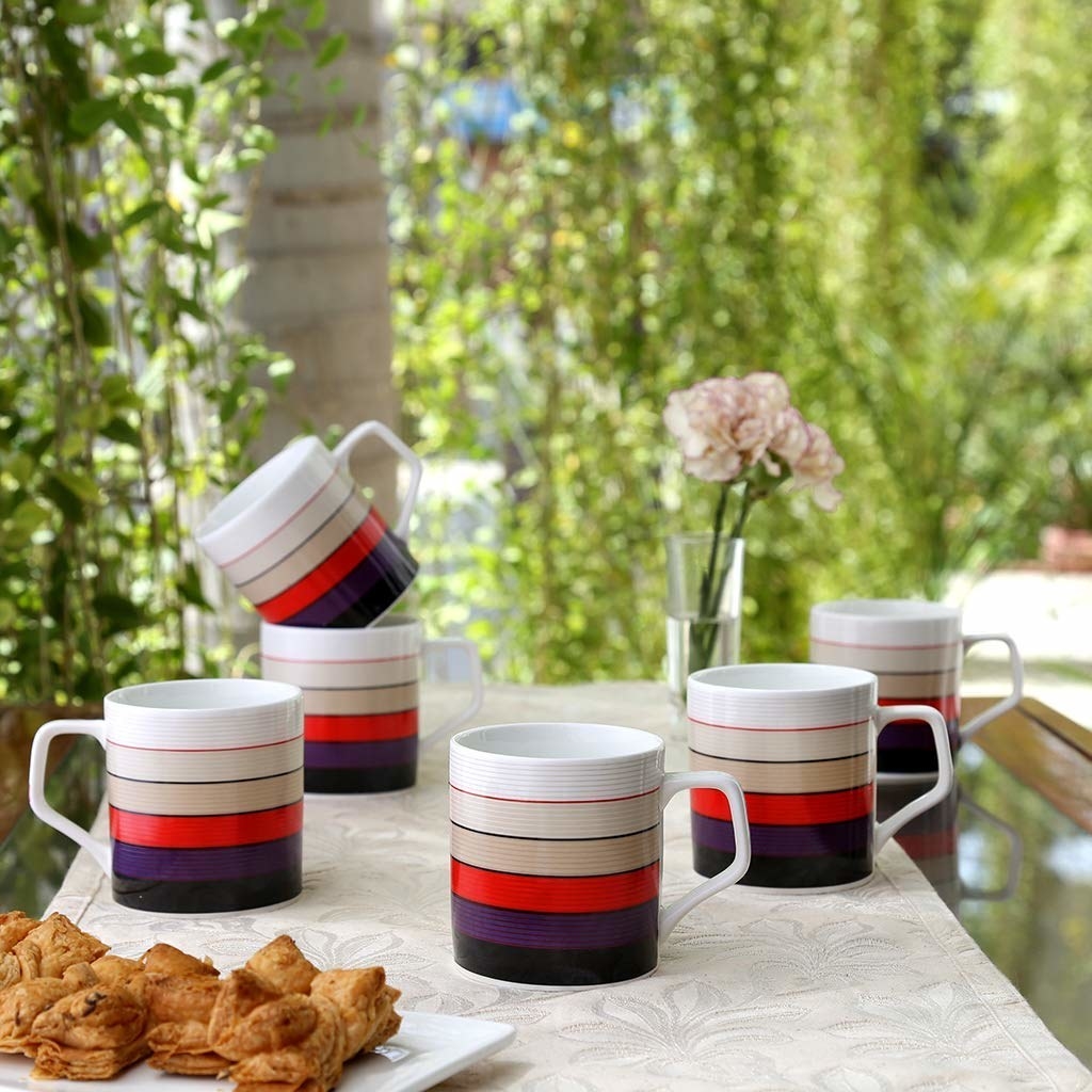 A set of mugs with colourful stripes placed next to a plate of fried snacks