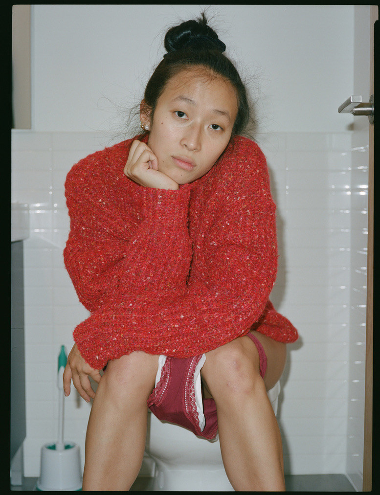 Nadya sits on a toilet with her underwear down, showing a pad